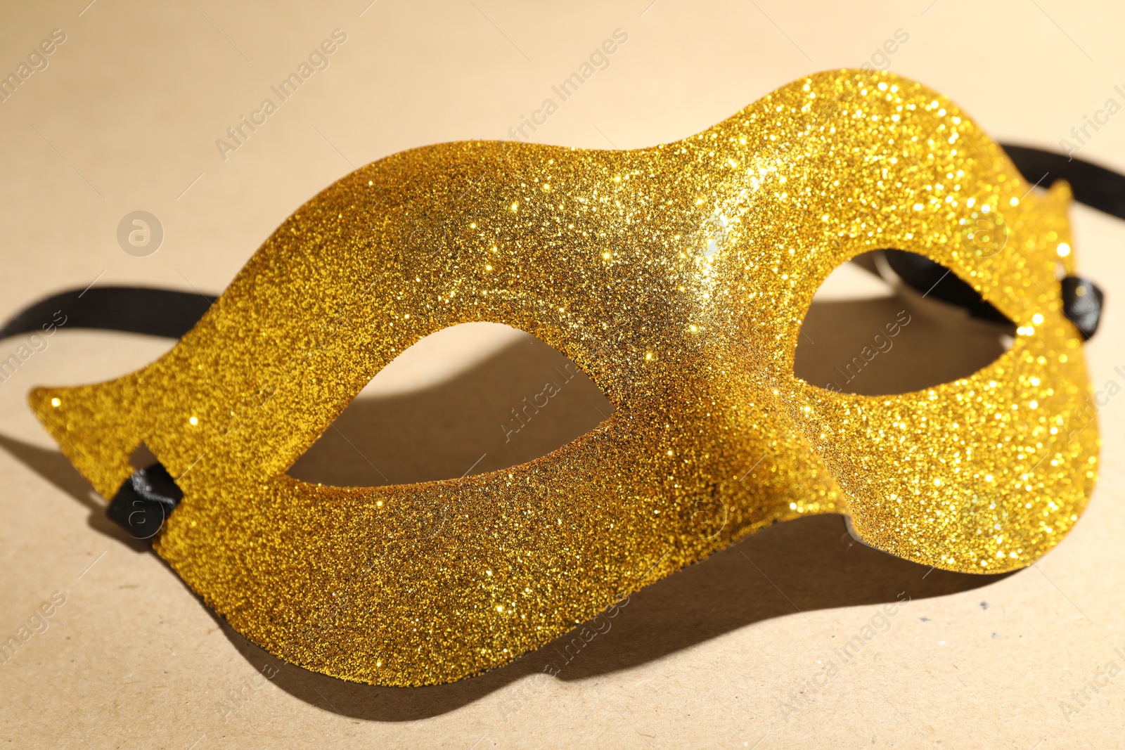 Photo of Beautiful golden carnival mask on beige background, closeup