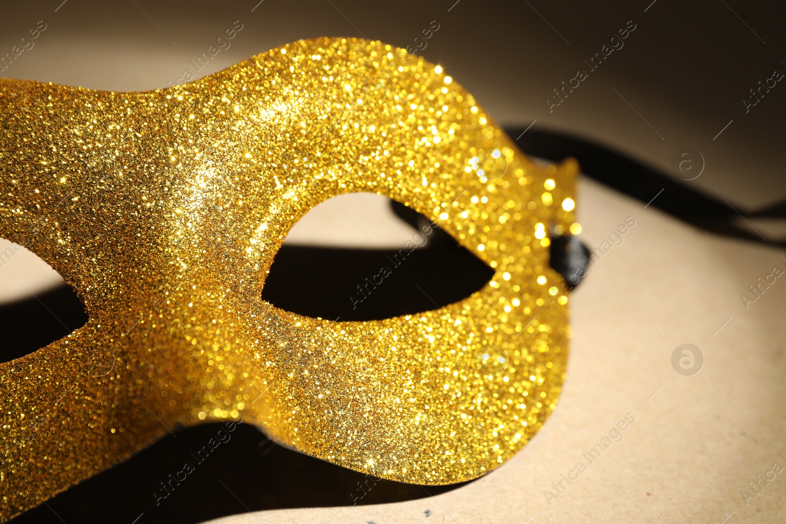 Photo of Beautiful golden carnival mask on beige background, closeup