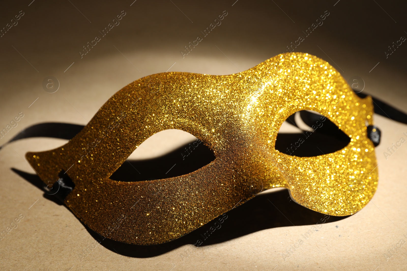 Photo of Beautiful golden carnival mask on beige background, closeup