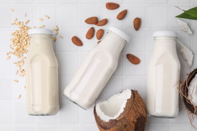 Photo of Different types of vegan milk in bottles and ingredients on white tiled table, flat lay