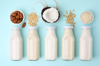 Photo of Different types of vegan milk in bottles and ingredients on light blue table, flat lay