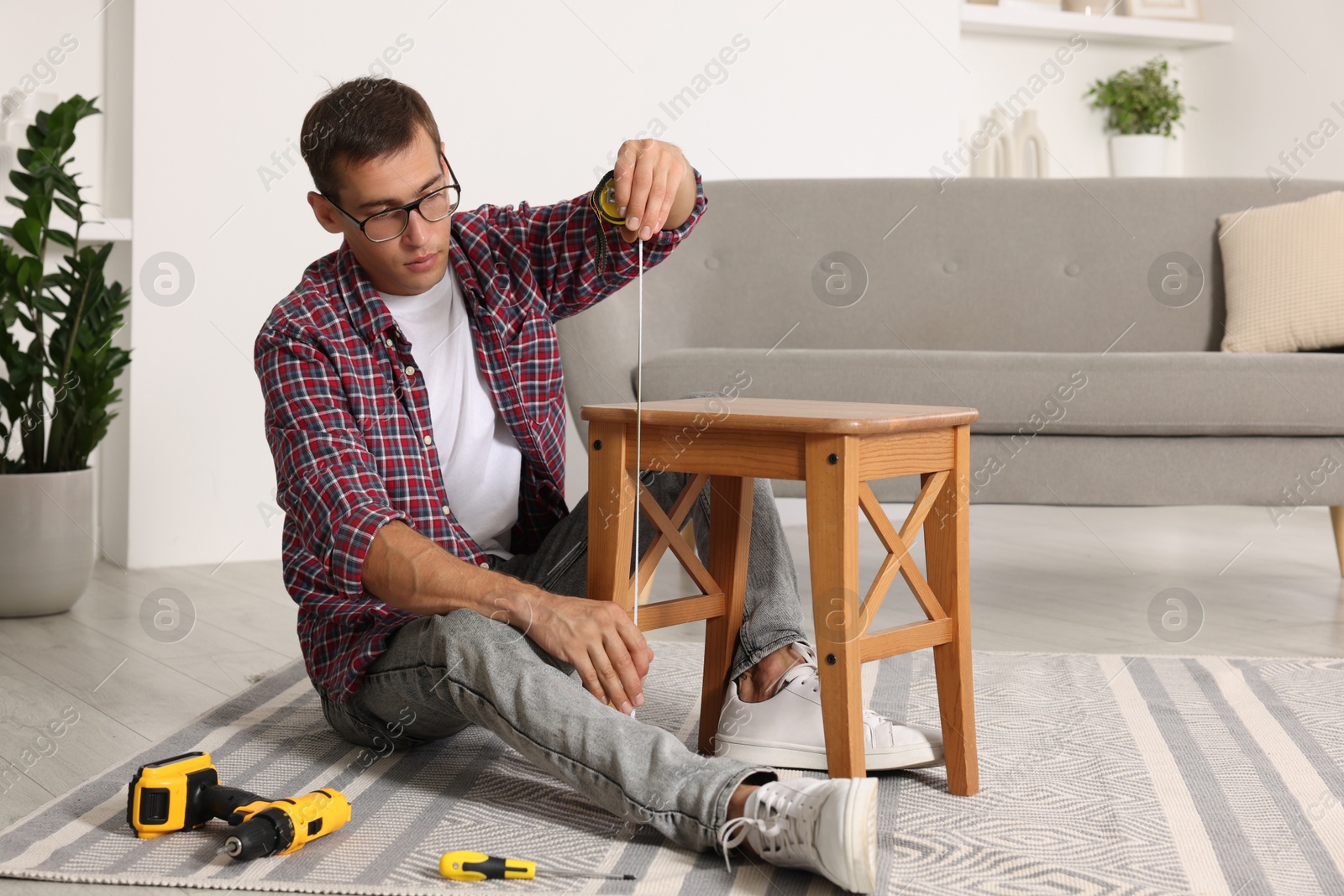 Photo of Man using tape measure while repairing wooden stool indoors