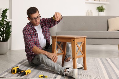 Photo of Man using tape measure while repairing wooden stool indoors