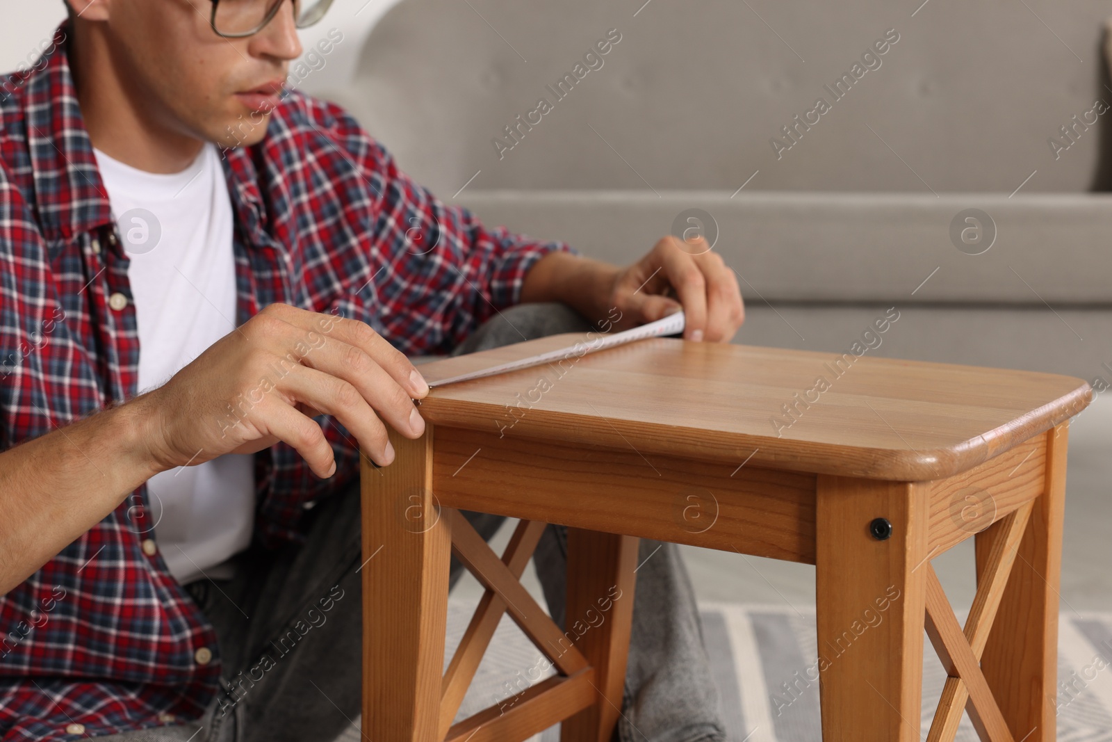 Photo of Man using tape measure while repairing wooden stool indoors, closeup