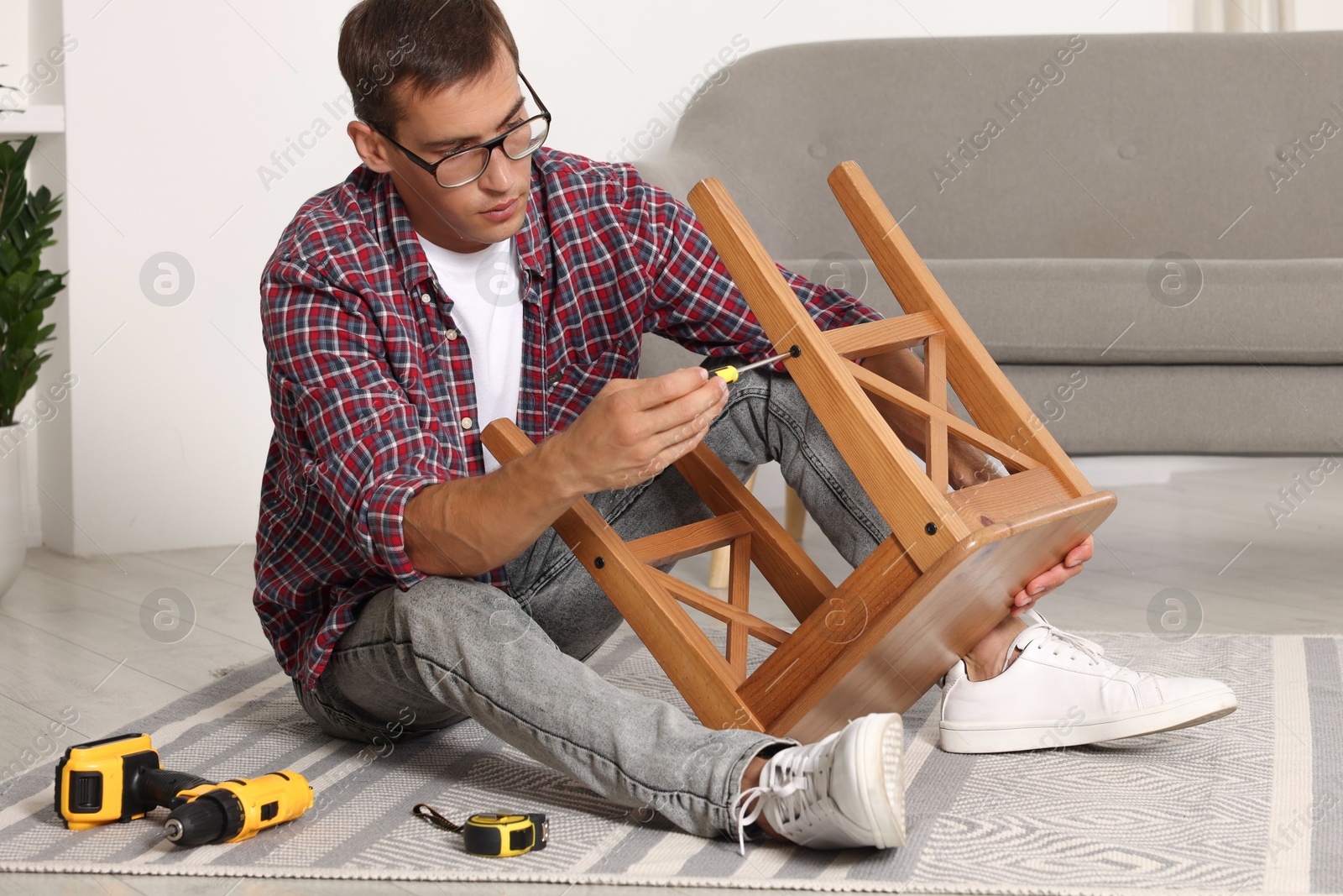 Photo of Man repairing wooden stool with screwdriver indoors