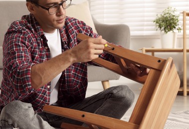 Man repairing wooden stool with screwdriver indoors