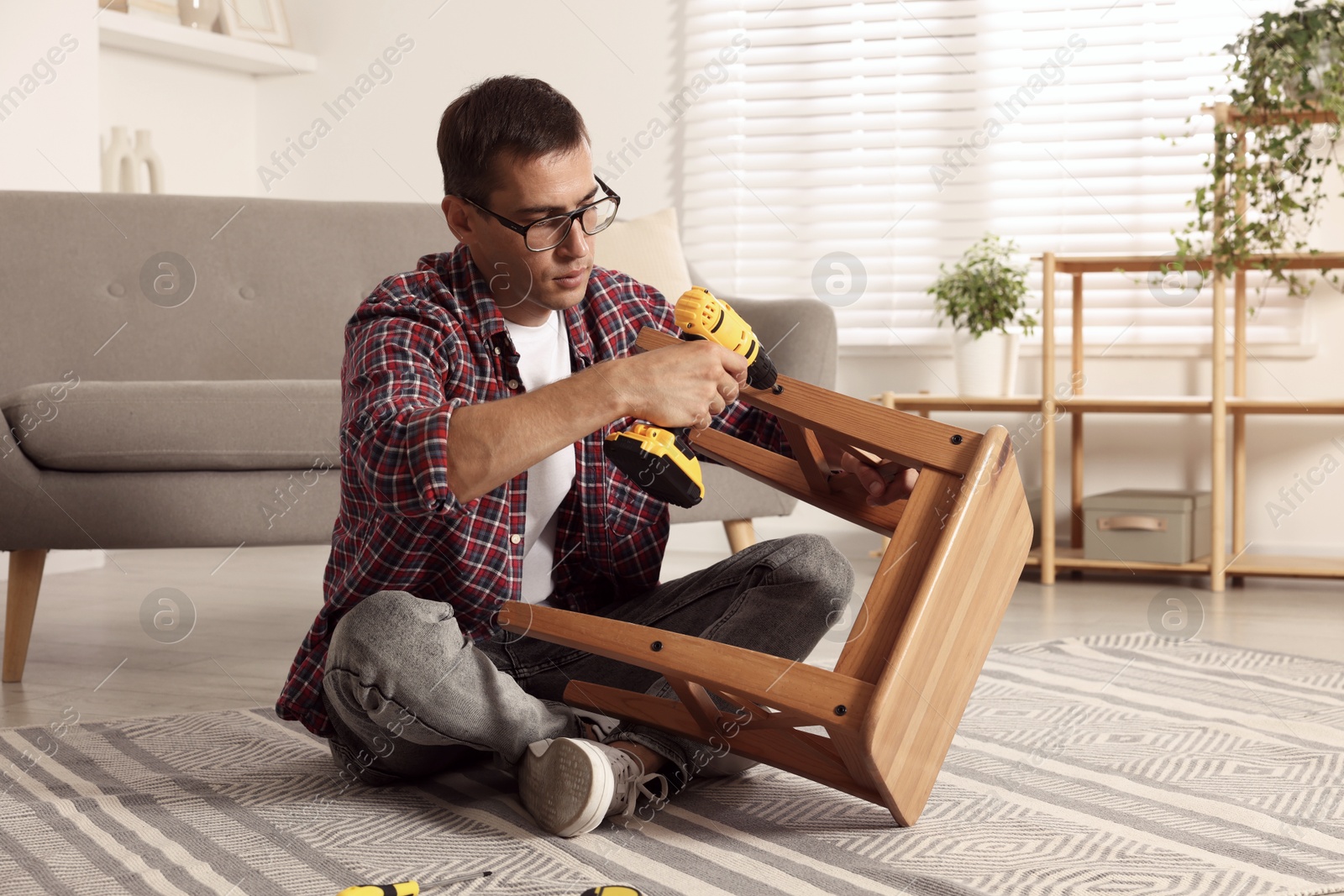 Photo of Man repairing wooden stool with electric screwdriver indoors