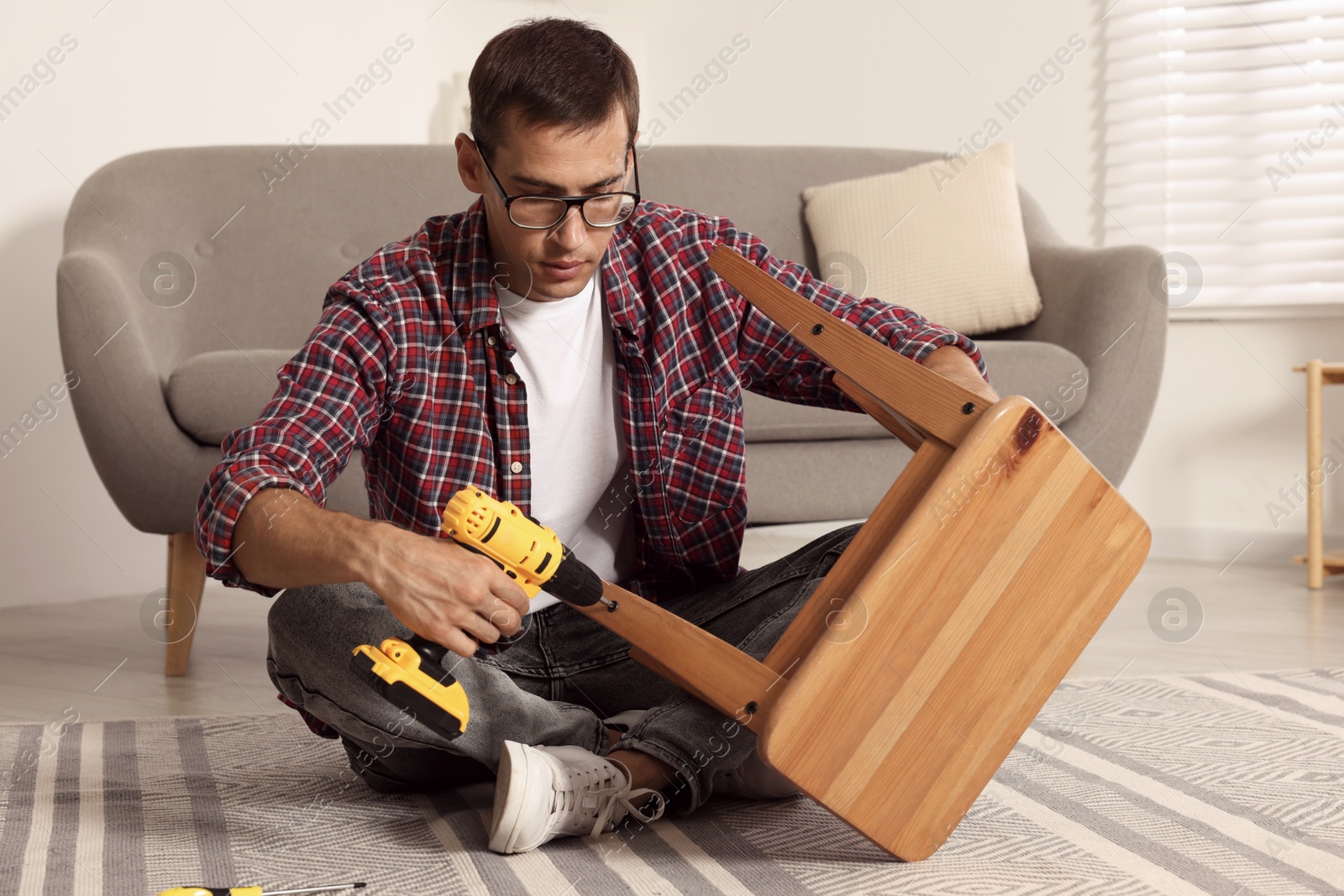 Photo of Man repairing wooden stool with electric screwdriver indoors