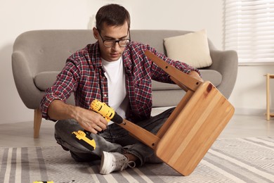 Man repairing wooden stool with electric screwdriver indoors