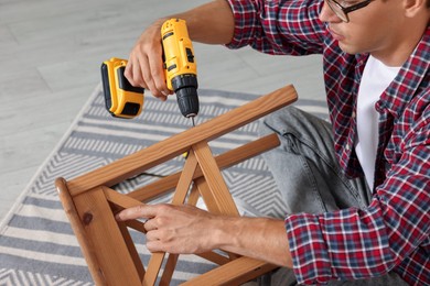 Man repairing wooden stool with electric screwdriver indoors, closeup