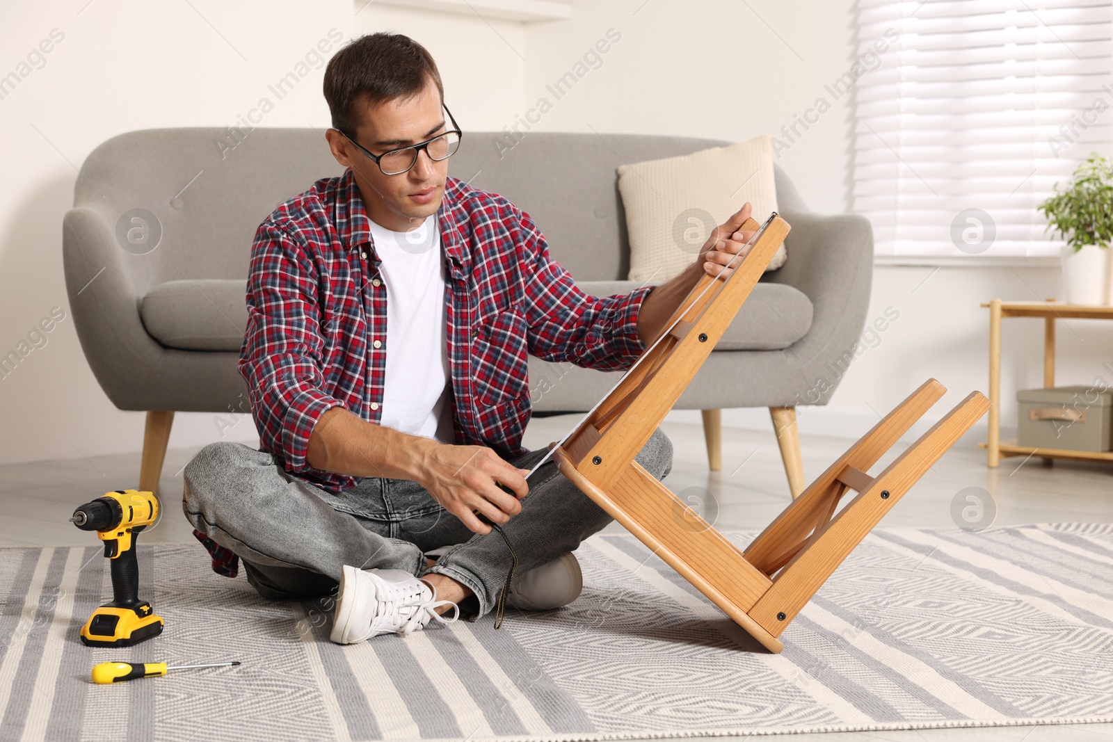 Photo of Man using tape measure while repairing wooden stool indoors