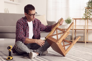 Photo of Man using tape measure while repairing wooden stool indoors