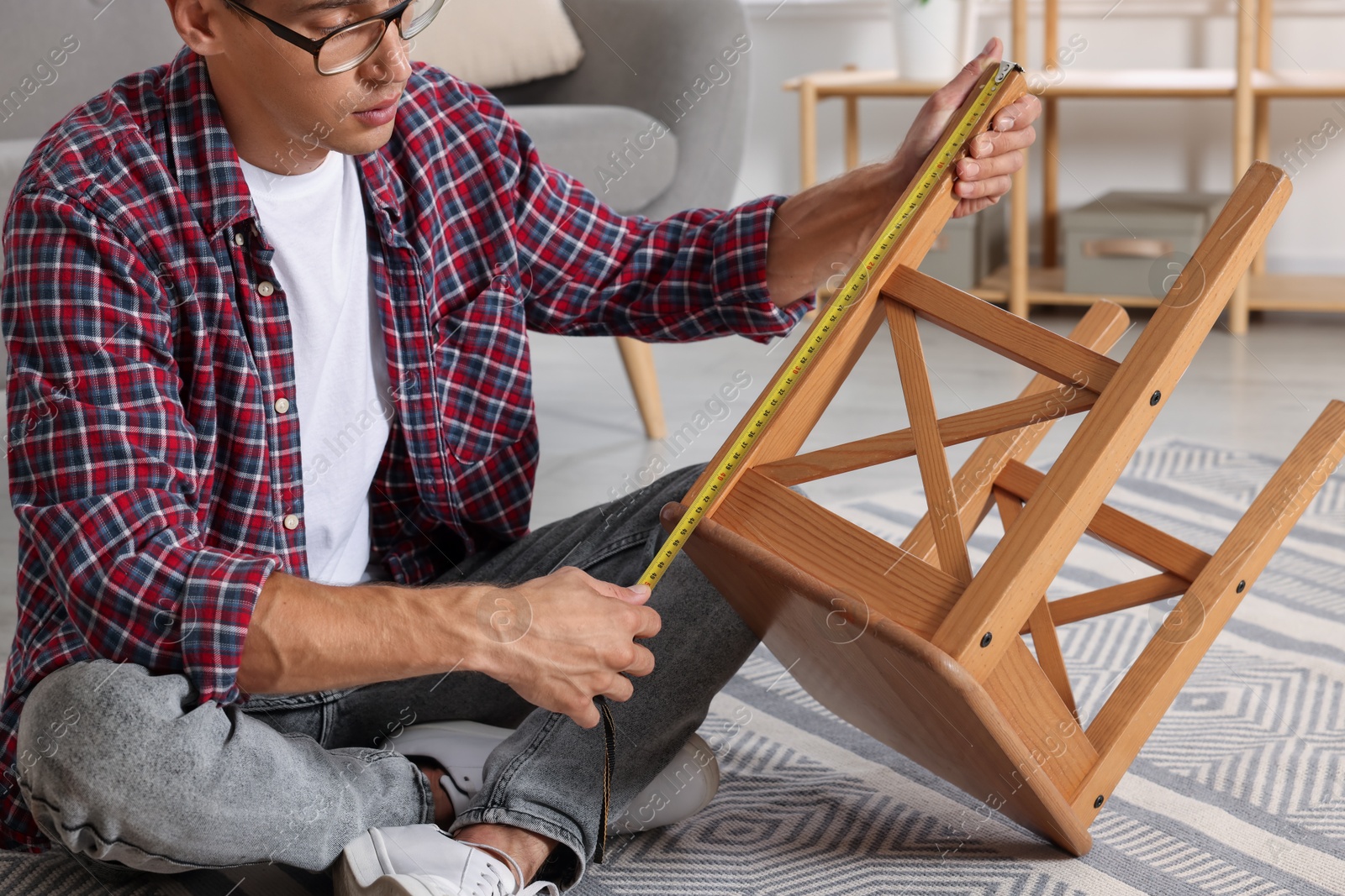 Photo of Man using tape measure while repairing wooden stool indoors