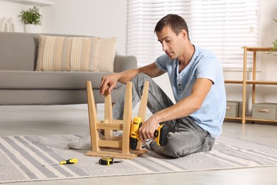 Photo of Man repairing wooden stool with electric screwdriver indoors