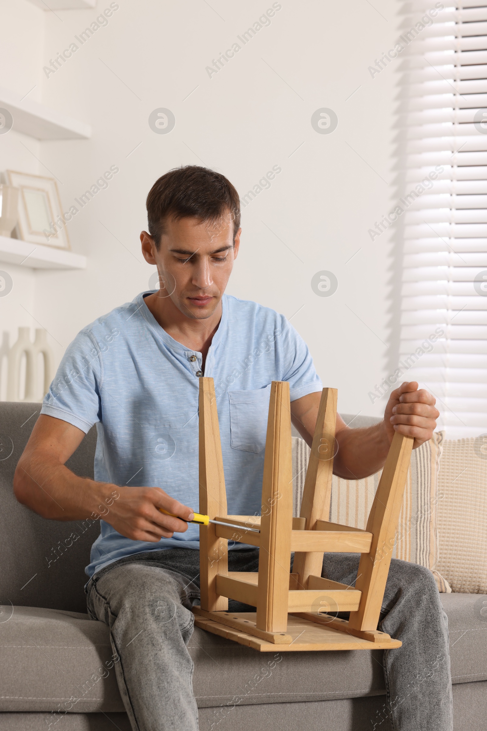 Photo of Man repairing wooden stool with screwdriver indoors