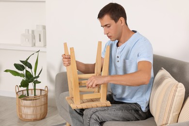 Photo of Man repairing wooden stool with screwdriver indoors