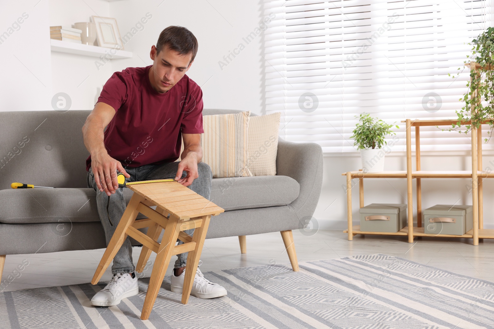 Photo of Man using tape measure while repairing wooden stool indoors