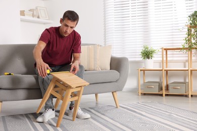 Man using tape measure while repairing wooden stool indoors