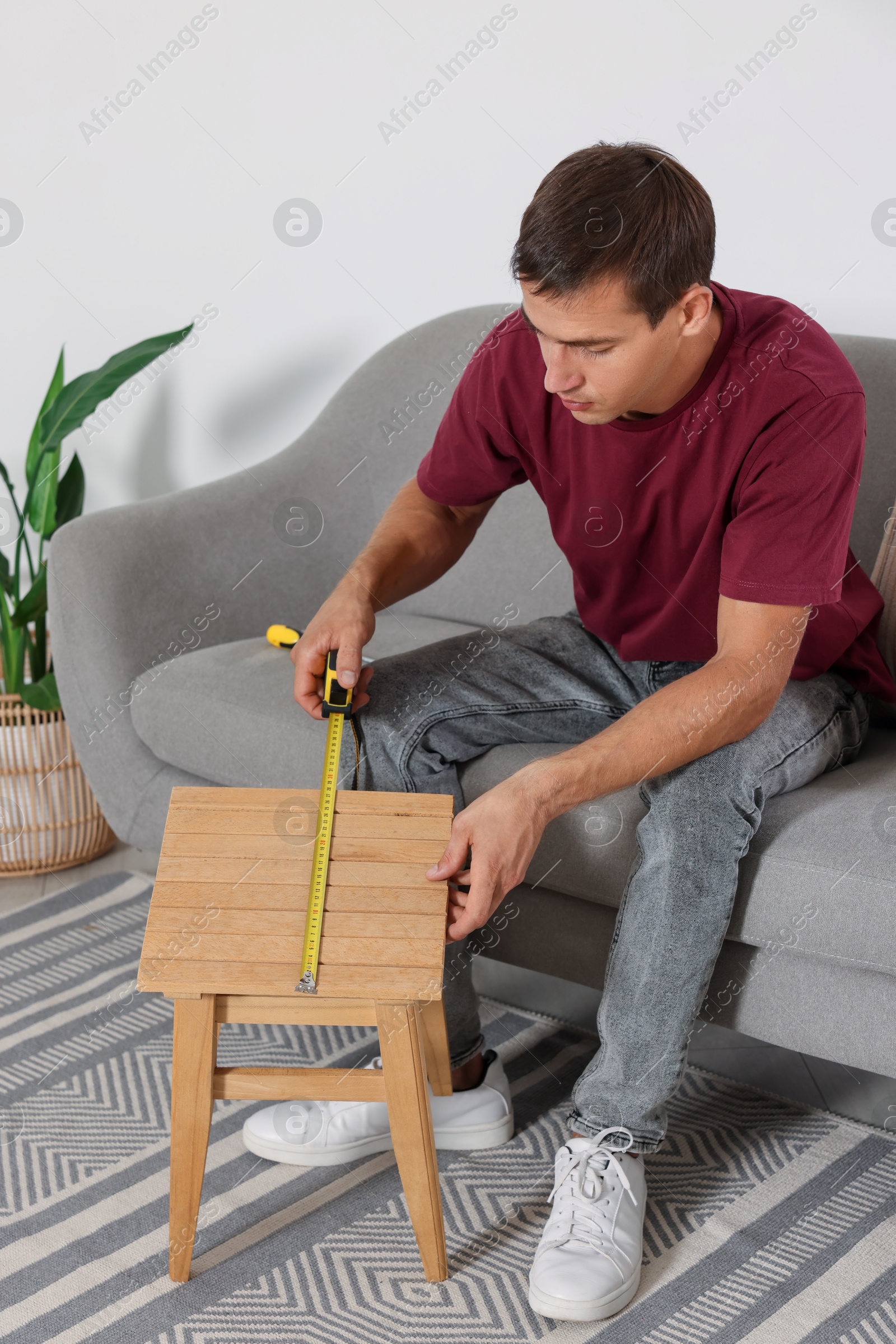 Photo of Man using tape measure while repairing wooden stool indoors