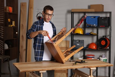 Photo of Man repairing wooden stool with screwdriver indoors