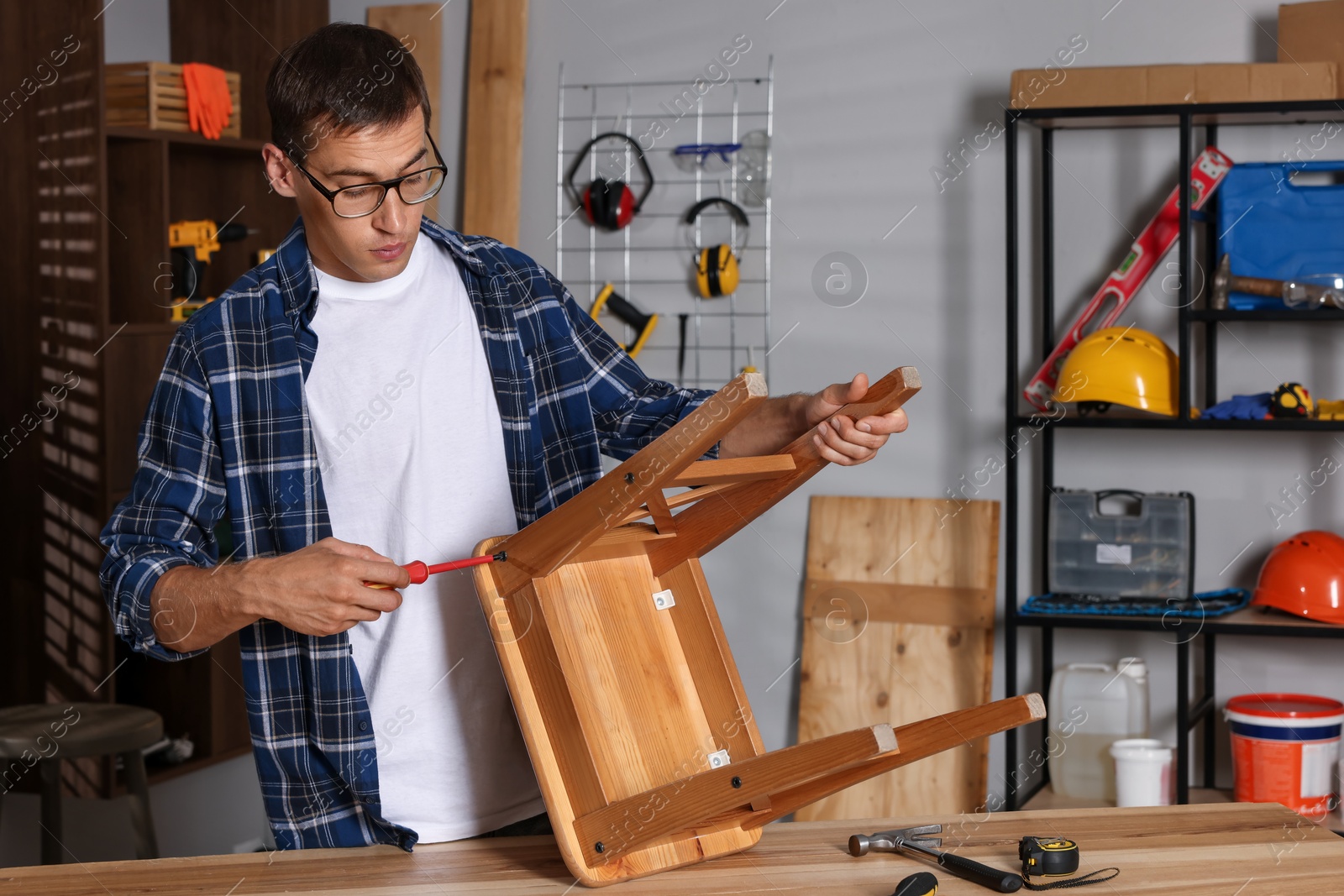 Photo of Man repairing wooden stool with screwdriver indoors