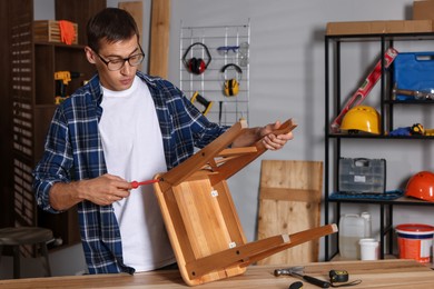 Man repairing wooden stool with screwdriver indoors