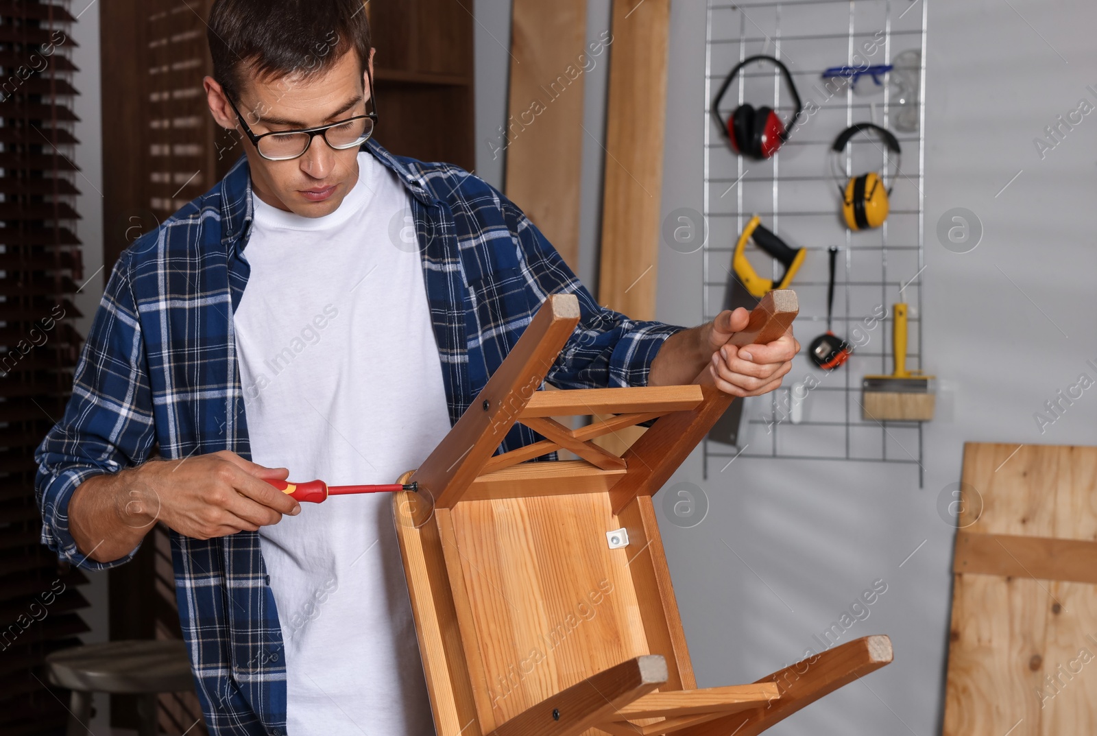 Photo of Man repairing wooden stool with screwdriver indoors