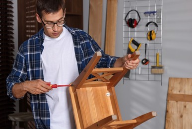 Man repairing wooden stool with screwdriver indoors