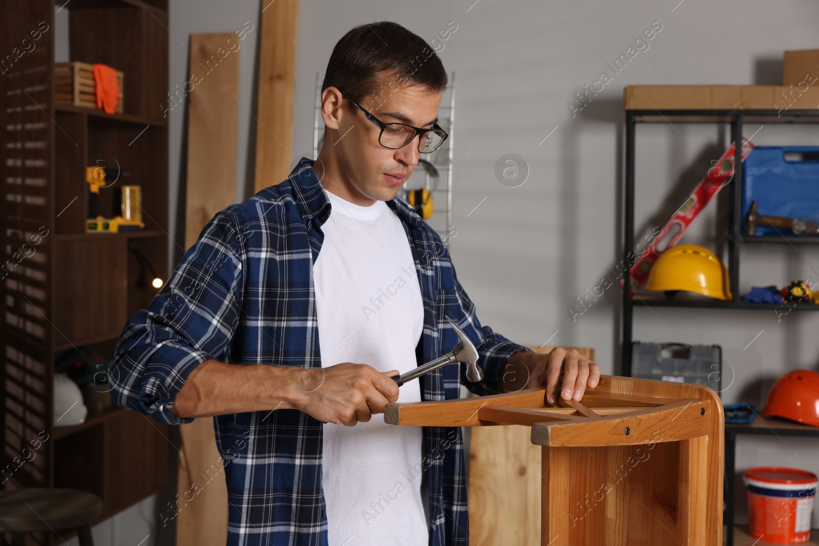 Photo of Man repairing wooden stool with hammer indoors