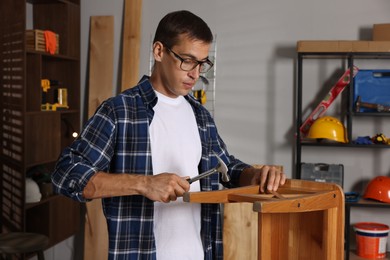 Man repairing wooden stool with hammer indoors