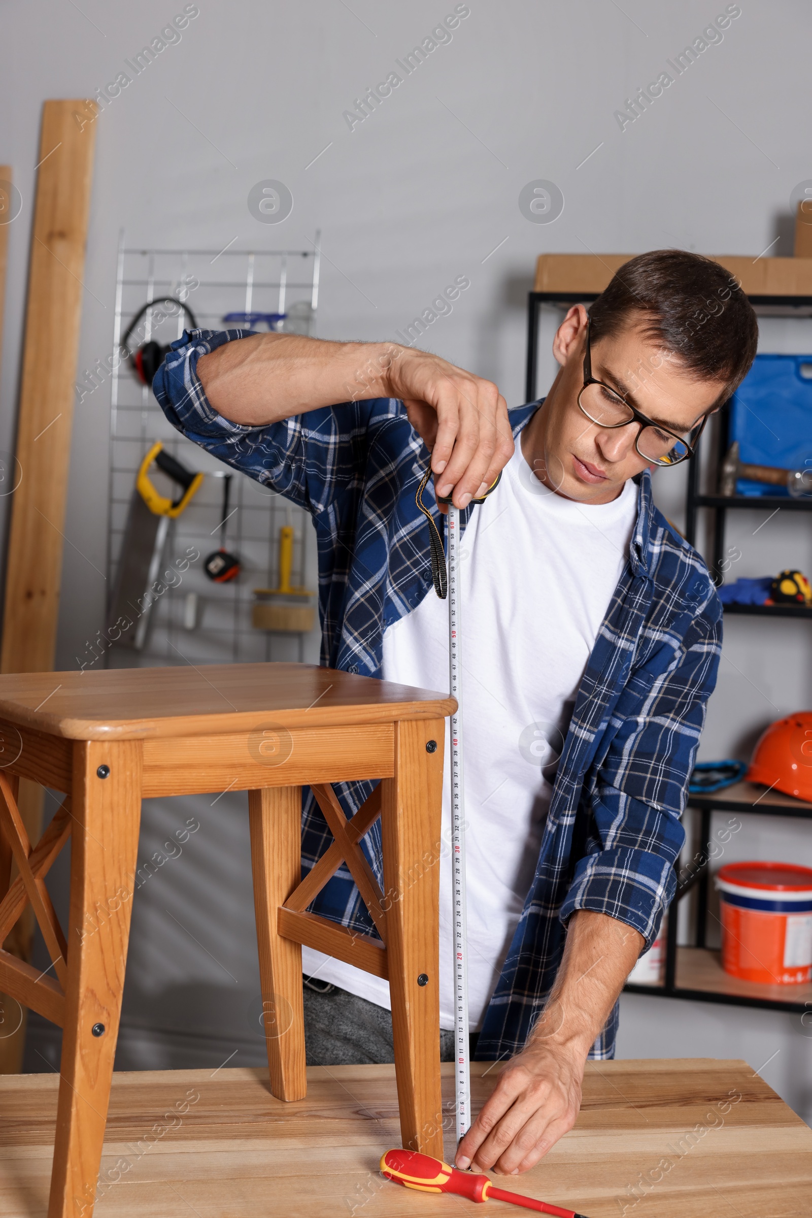 Photo of Man using tape measure while repairing wooden stool indoors