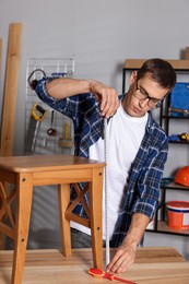 Man using tape measure while repairing wooden stool indoors