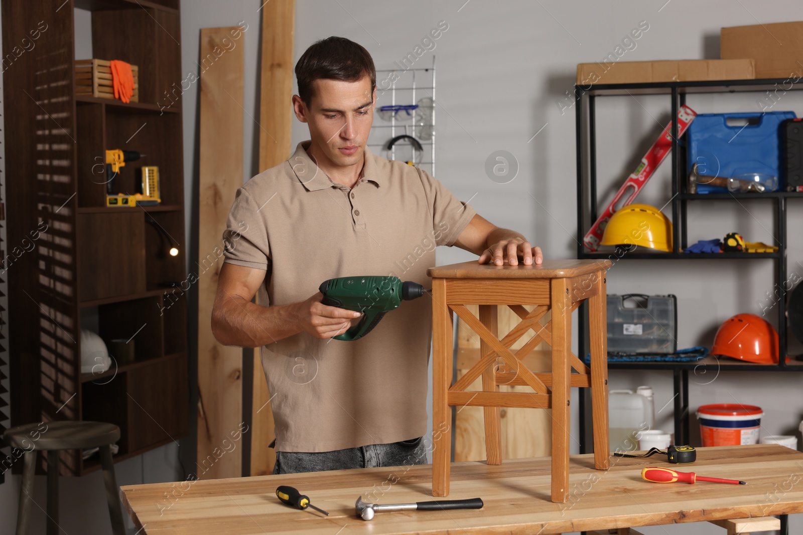 Photo of Man repairing wooden stool with electric screwdriver indoors