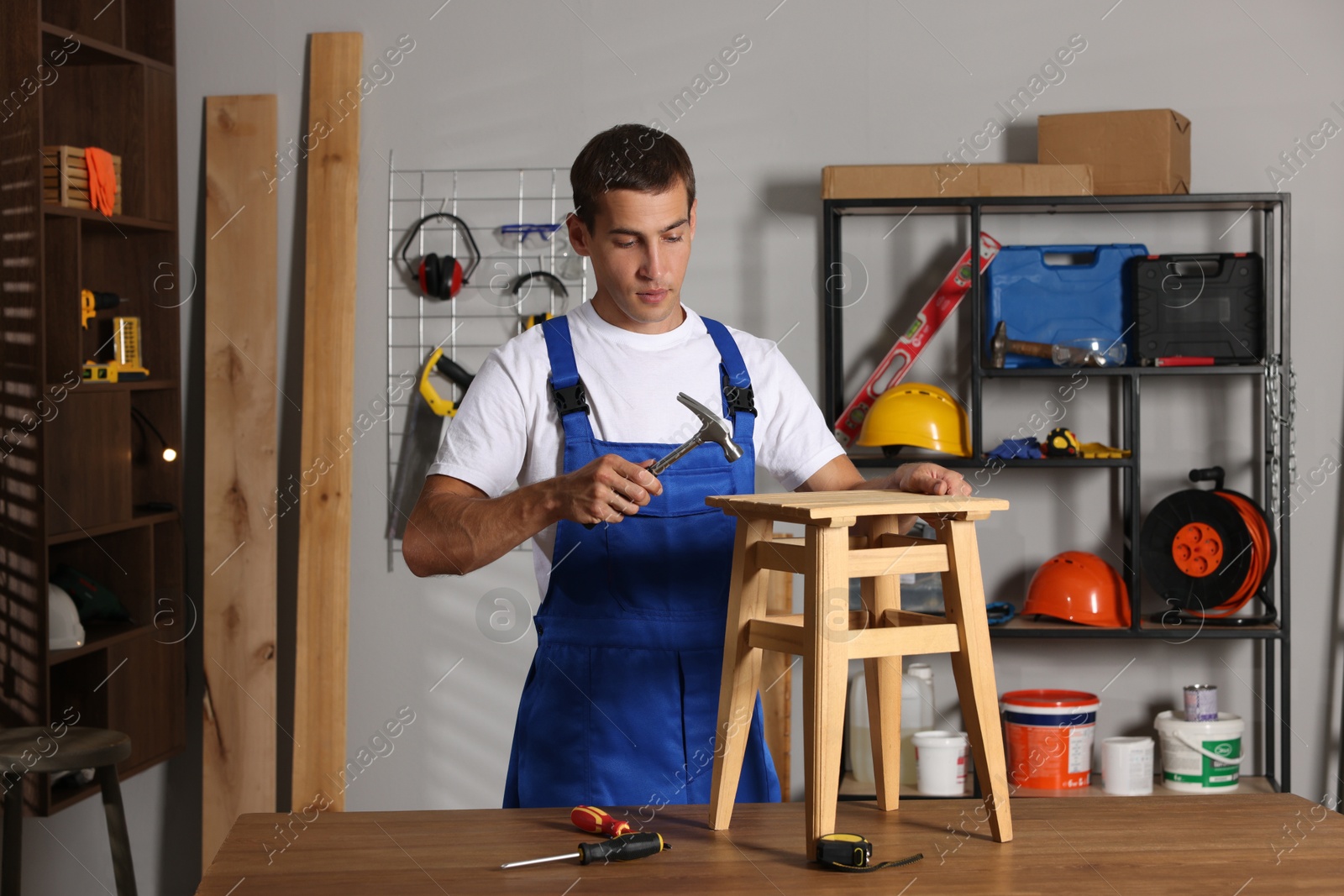 Photo of Man repairing wooden stool with hammer indoors