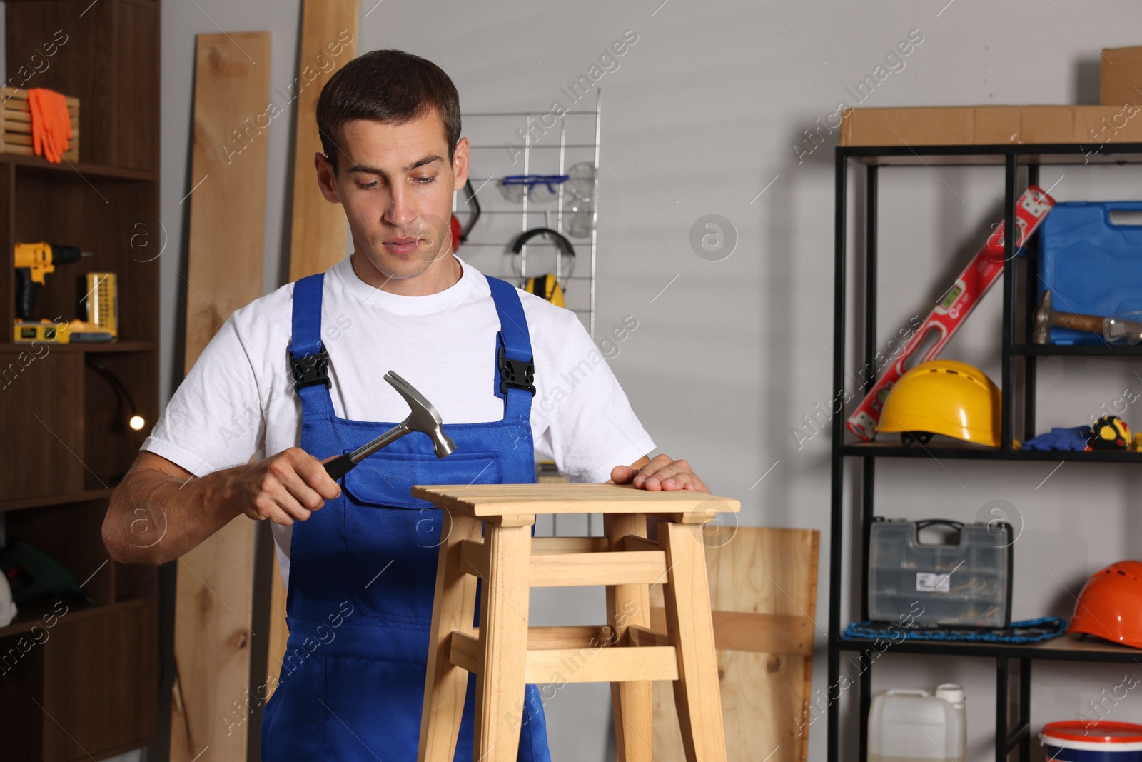 Photo of Man repairing wooden stool with hammer indoors