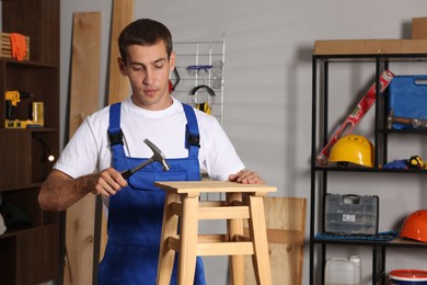 Photo of Man repairing wooden stool with hammer indoors