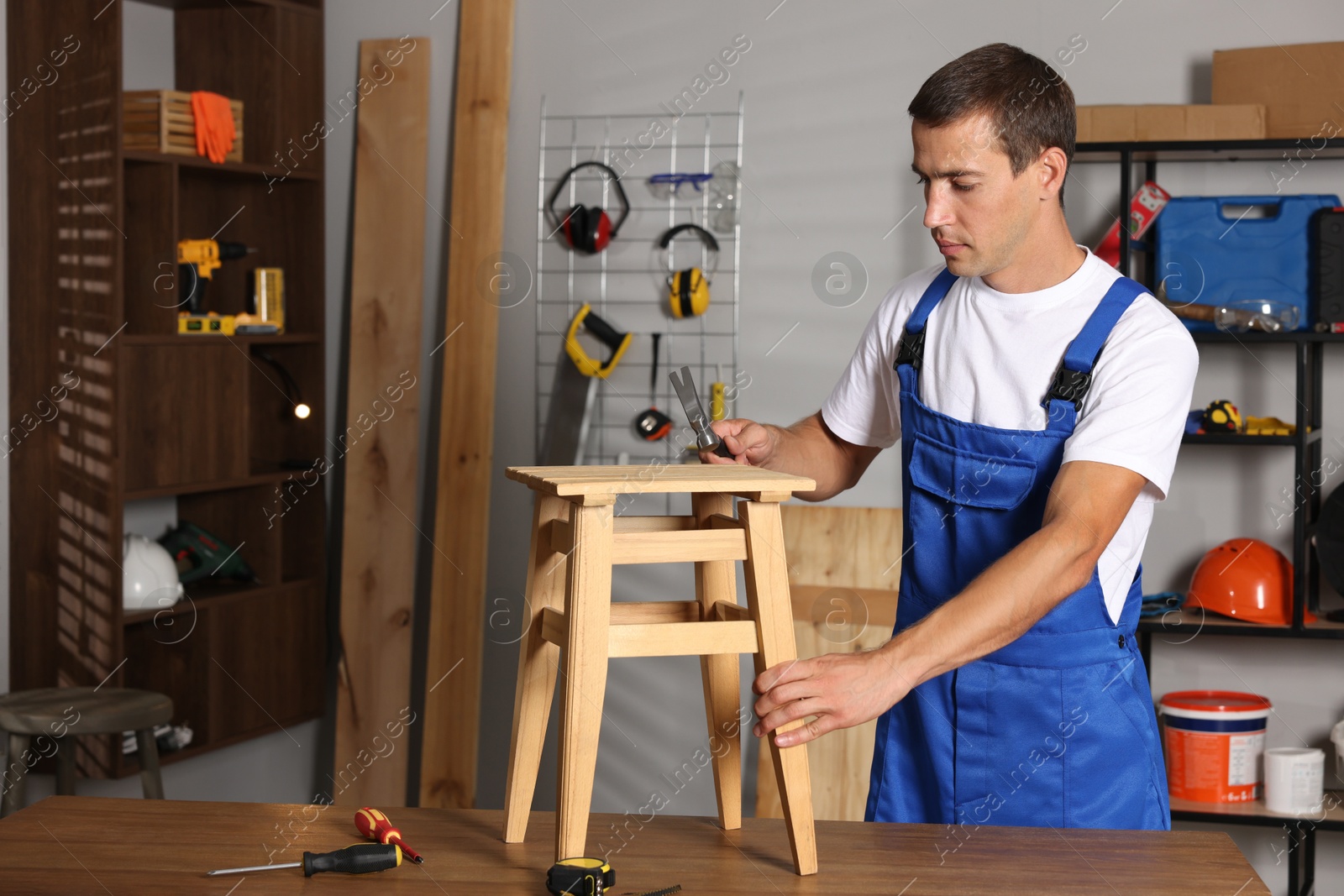 Photo of Man repairing wooden stool with hammer indoors