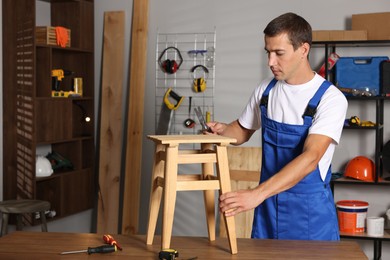 Photo of Man repairing wooden stool with hammer indoors