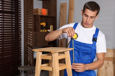 Man using tape measure while repairing wooden stool indoors