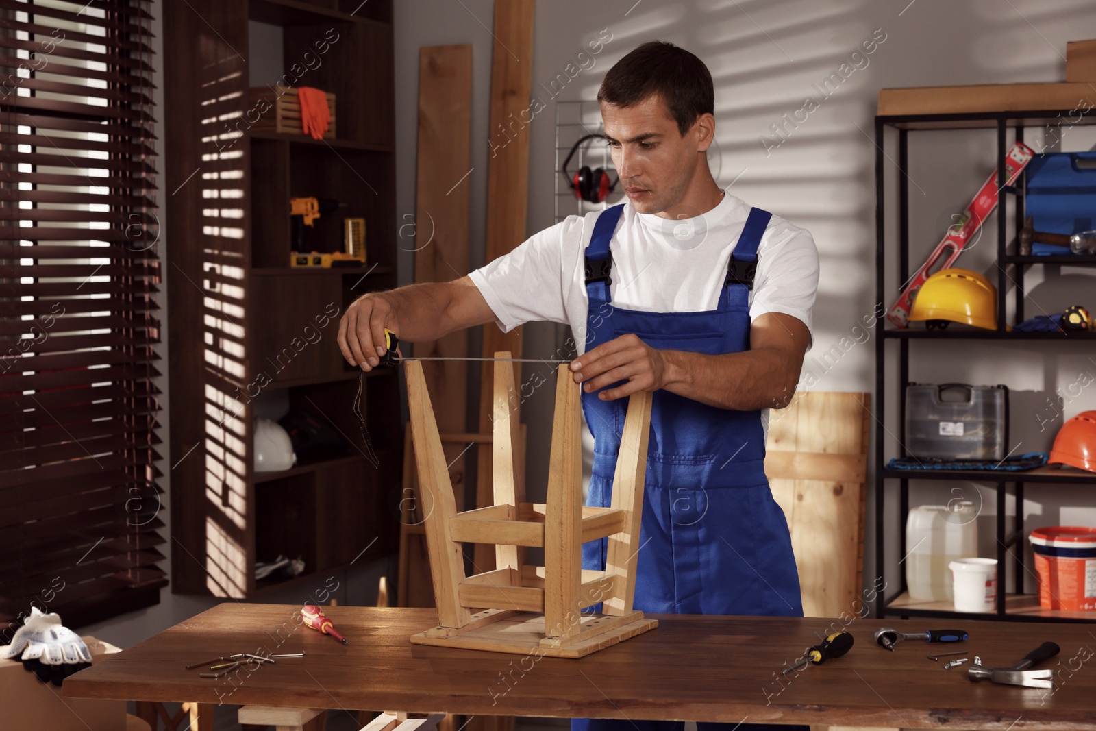 Photo of Man using tape measure while repairing wooden stool indoors