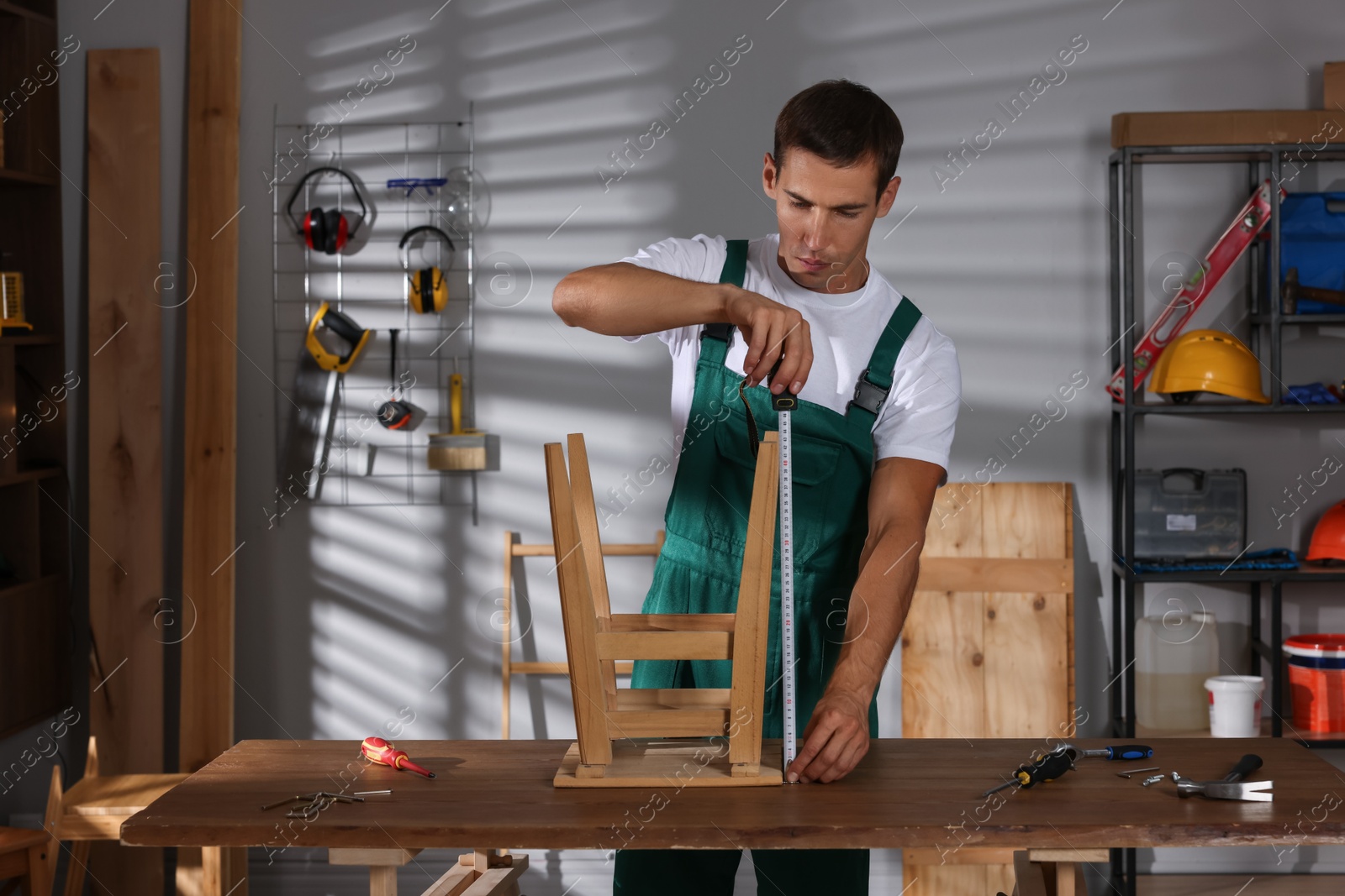 Photo of Man using tape measure while repairing wooden stool indoors