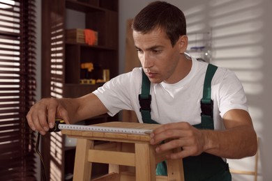 Man using tape measure while repairing wooden stool indoors