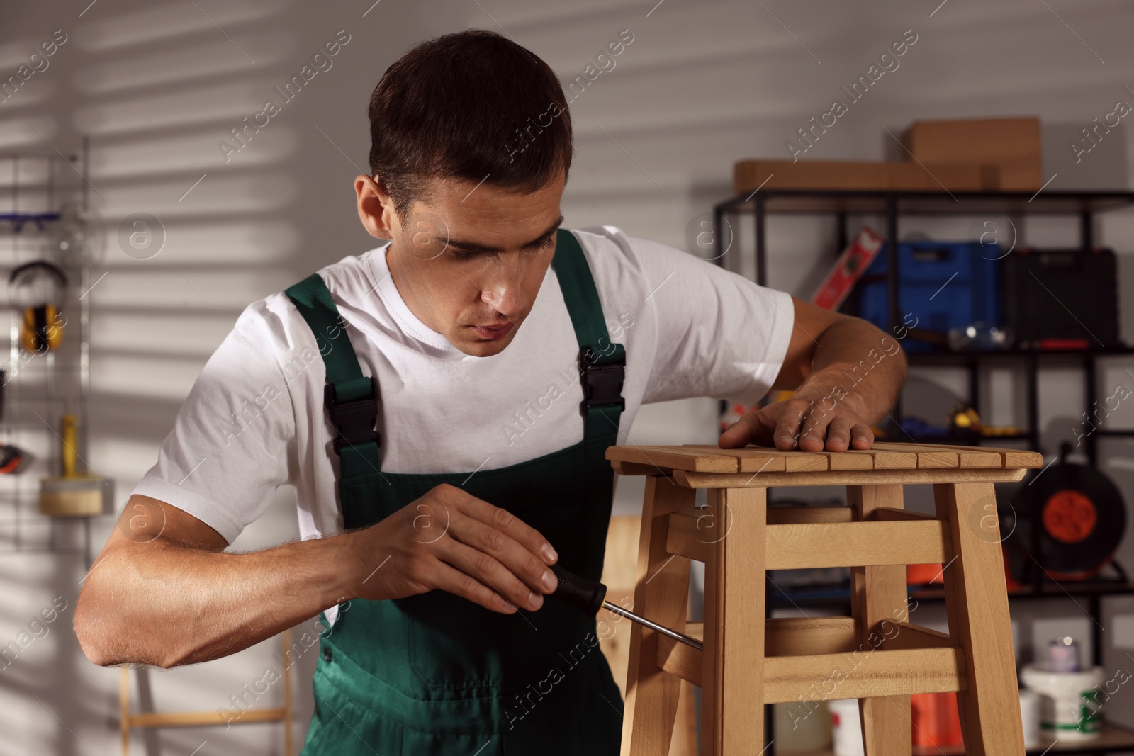 Photo of Man repairing wooden stool with screwdriver indoors