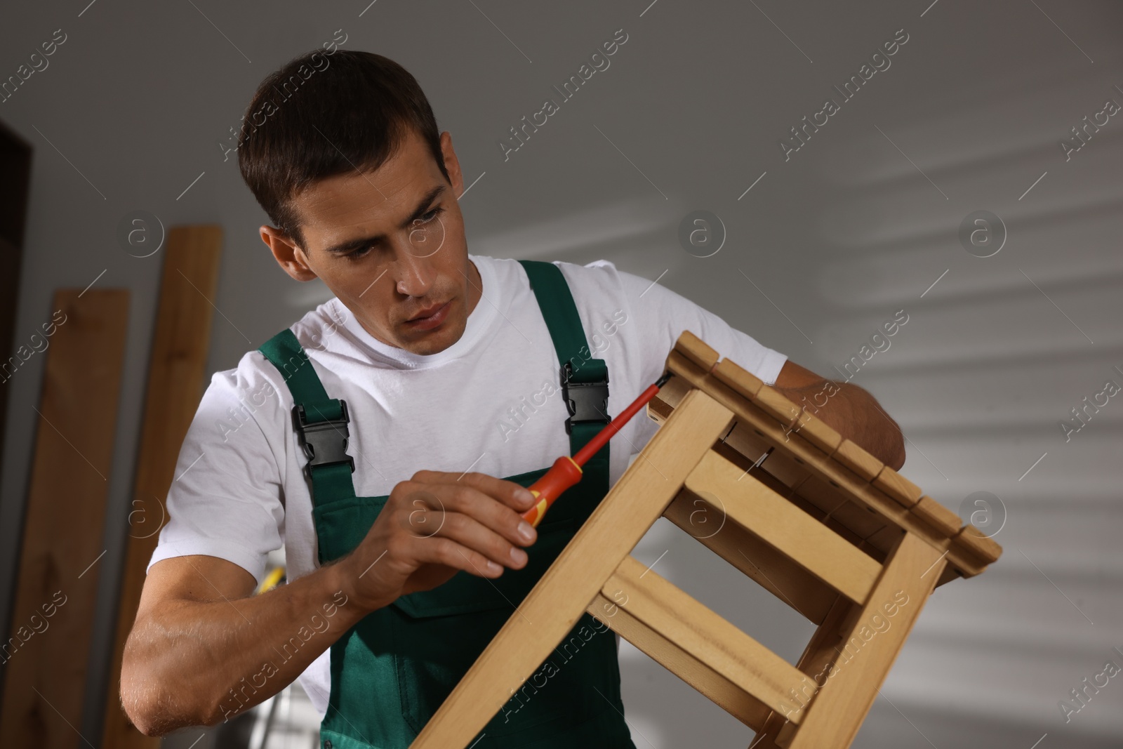 Photo of Man repairing wooden stool with screwdriver indoors