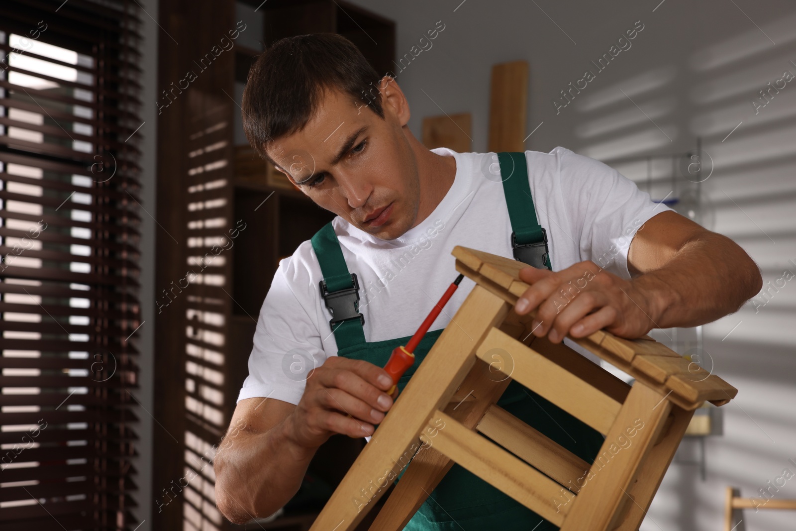 Photo of Man repairing wooden stool with screwdriver indoors