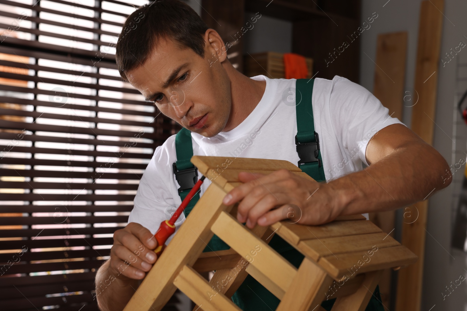 Photo of Man repairing wooden stool with screwdriver indoors