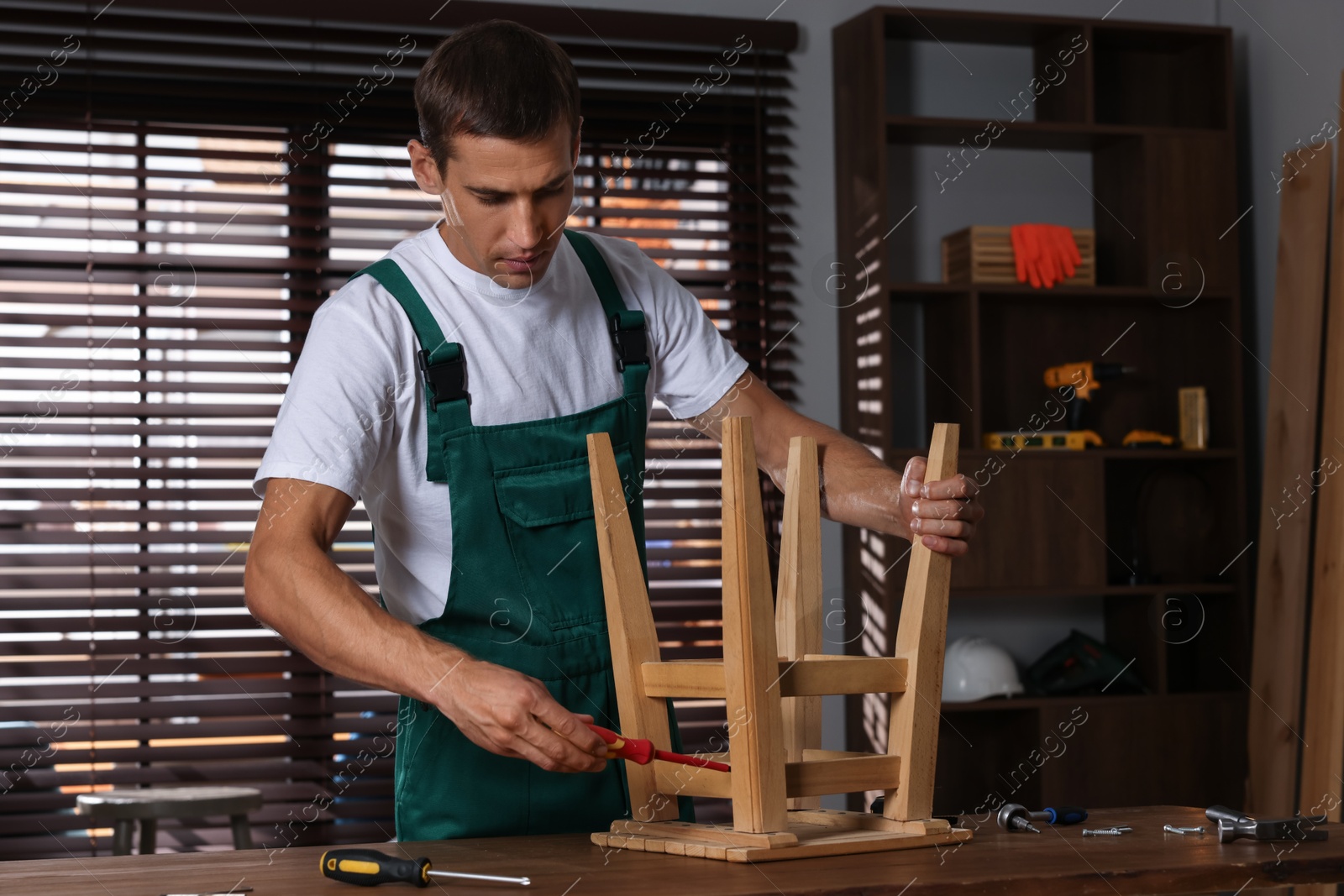 Photo of Man repairing wooden stool with screwdriver indoors