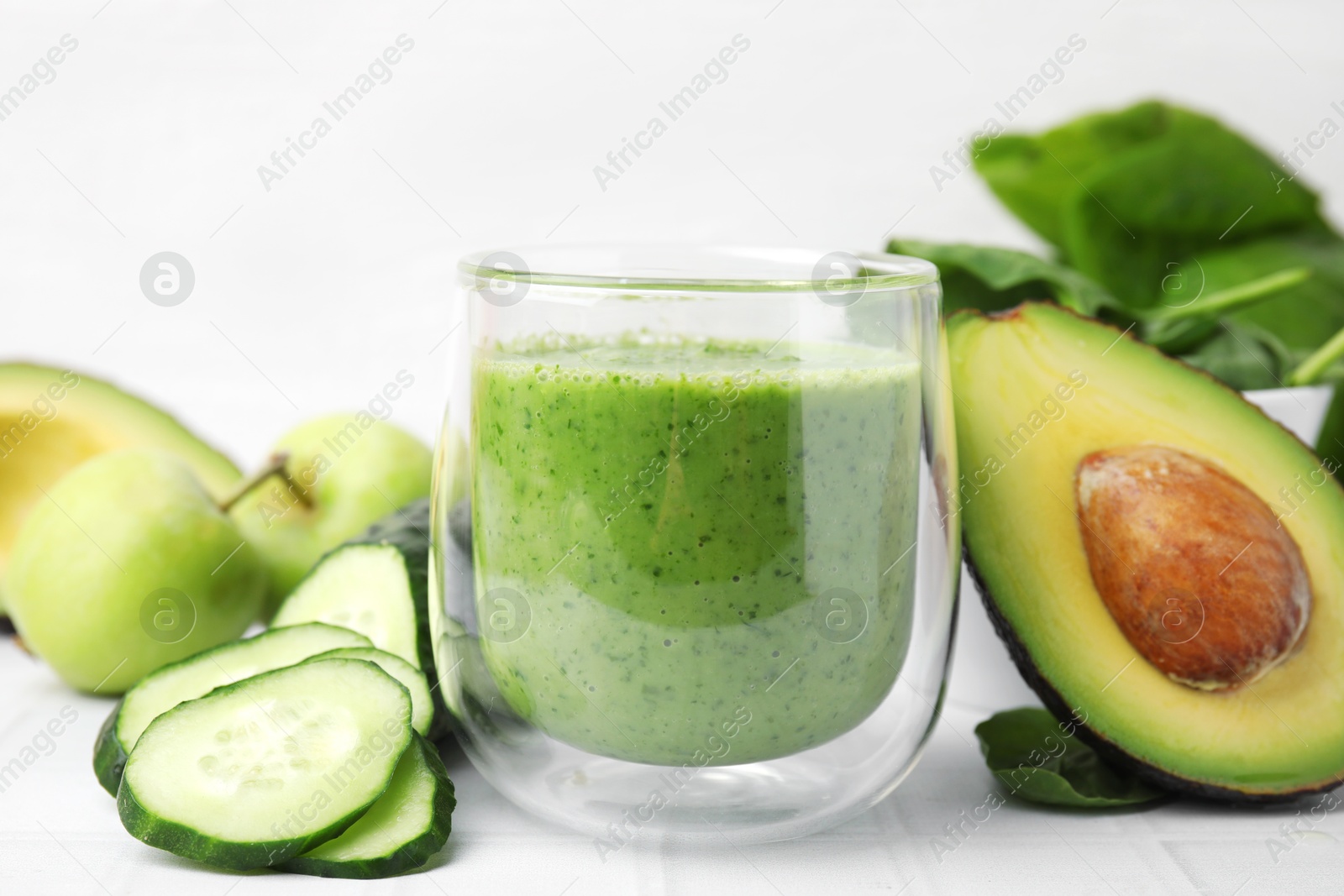 Photo of Tasty green smoothie in glass and products on white tiled table, closeup