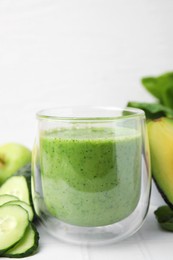 Photo of Tasty green smoothie in glass and products on white tiled table, closeup