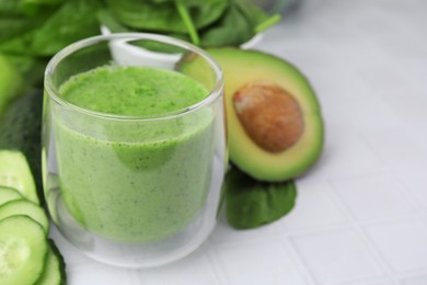 Photo of Tasty green smoothie in glass and products on white tiled table, closeup. Space for text